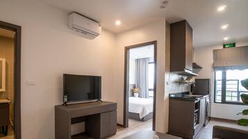 A modern hotel room with a flat-screen TV, a sink, a bed, a kitchenette, and a large window.