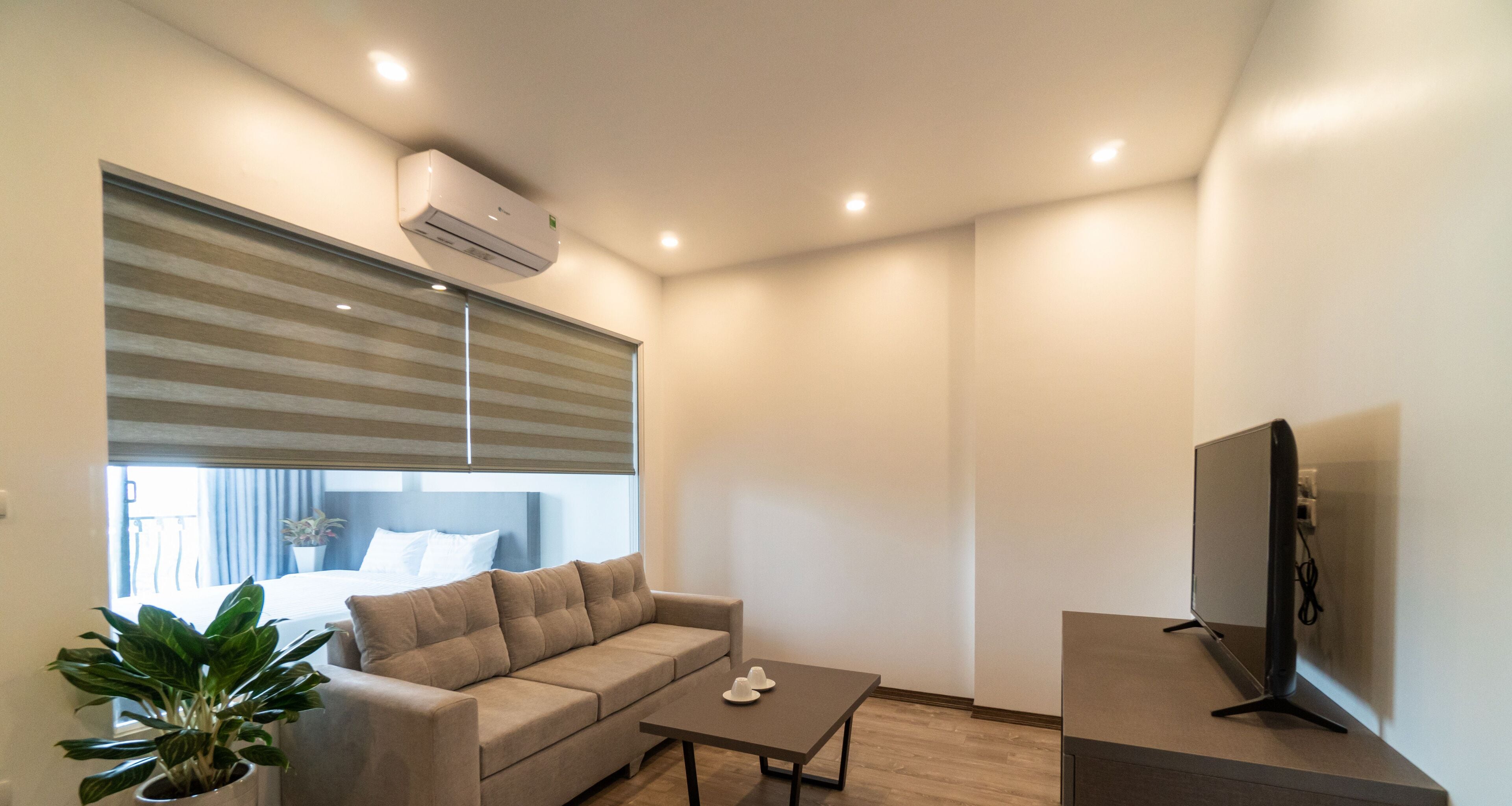 Uma sala de estar moderna com um sofá, uma mesa de centro, uma TV e uma janela grande com persianas.