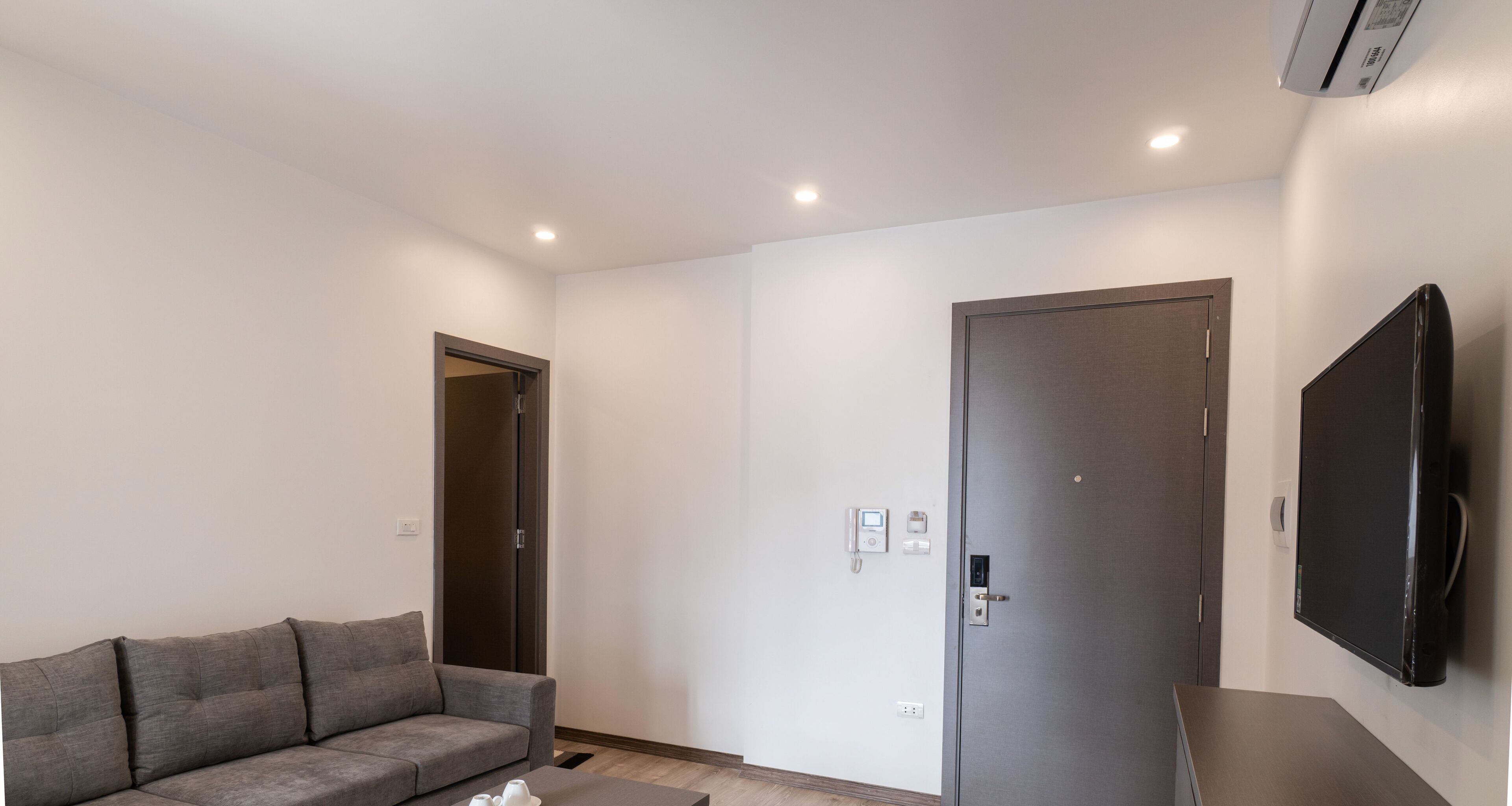 Un salon moderne avec un canapé gris, un téléviseur à écran plat fixé au mur et une porte dotée d’une serrure numérique.