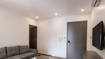 Un salon moderne avec un canapé gris, un téléviseur à écran plat fixé au mur et une porte dotée d’une serrure numérique.