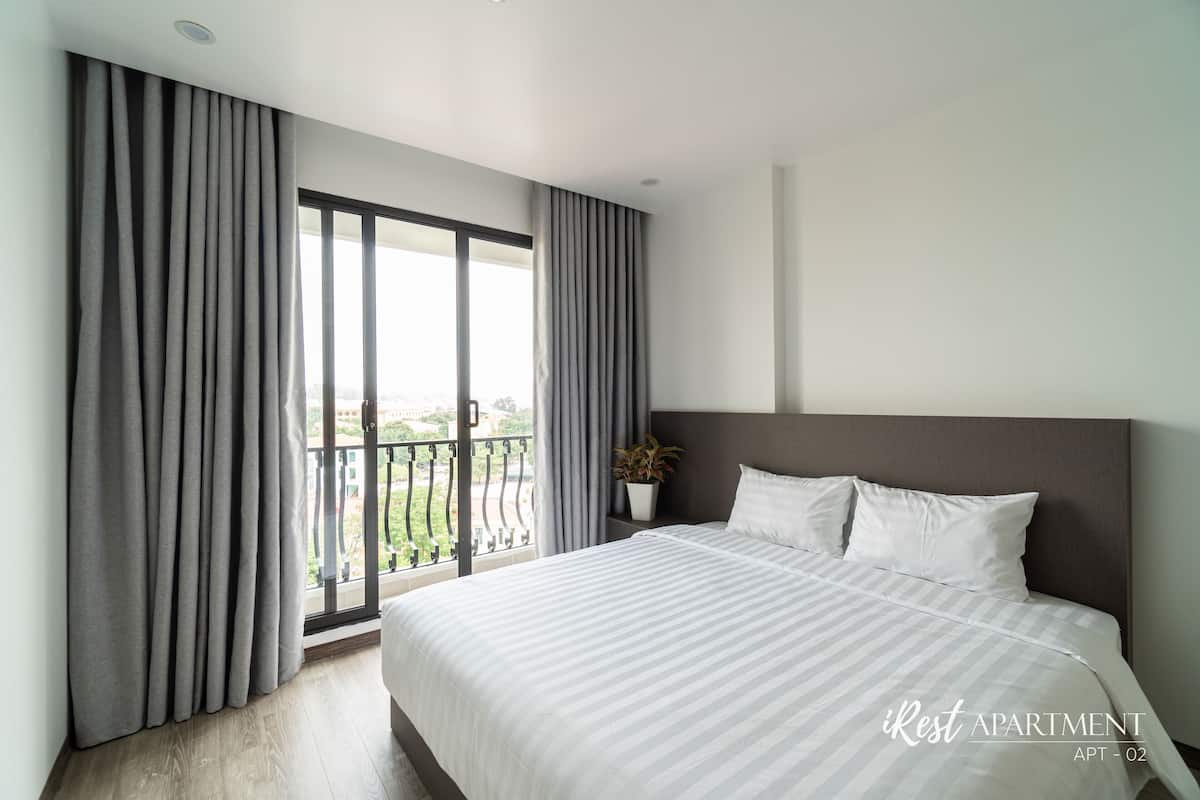 Une chambre moderne avec un grand lit, des rideaux gris, une plante en pot et une vue sur le balcon.