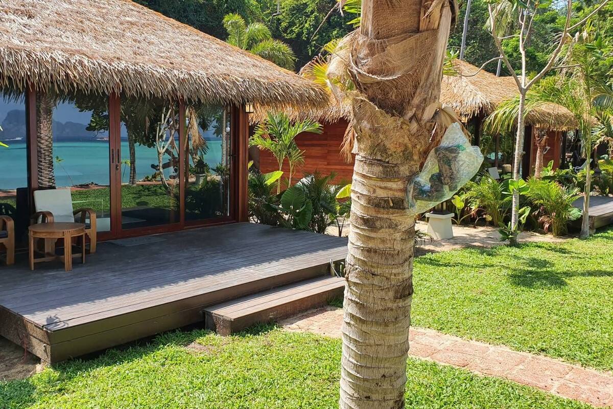 A thatched-roof structure with a wooden deck, surrounded by lush greenery and a view of the sea.