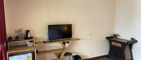 A compact living space with a television on a wooden stand, a small refrigerator, a trash bin, and a decorative console table.