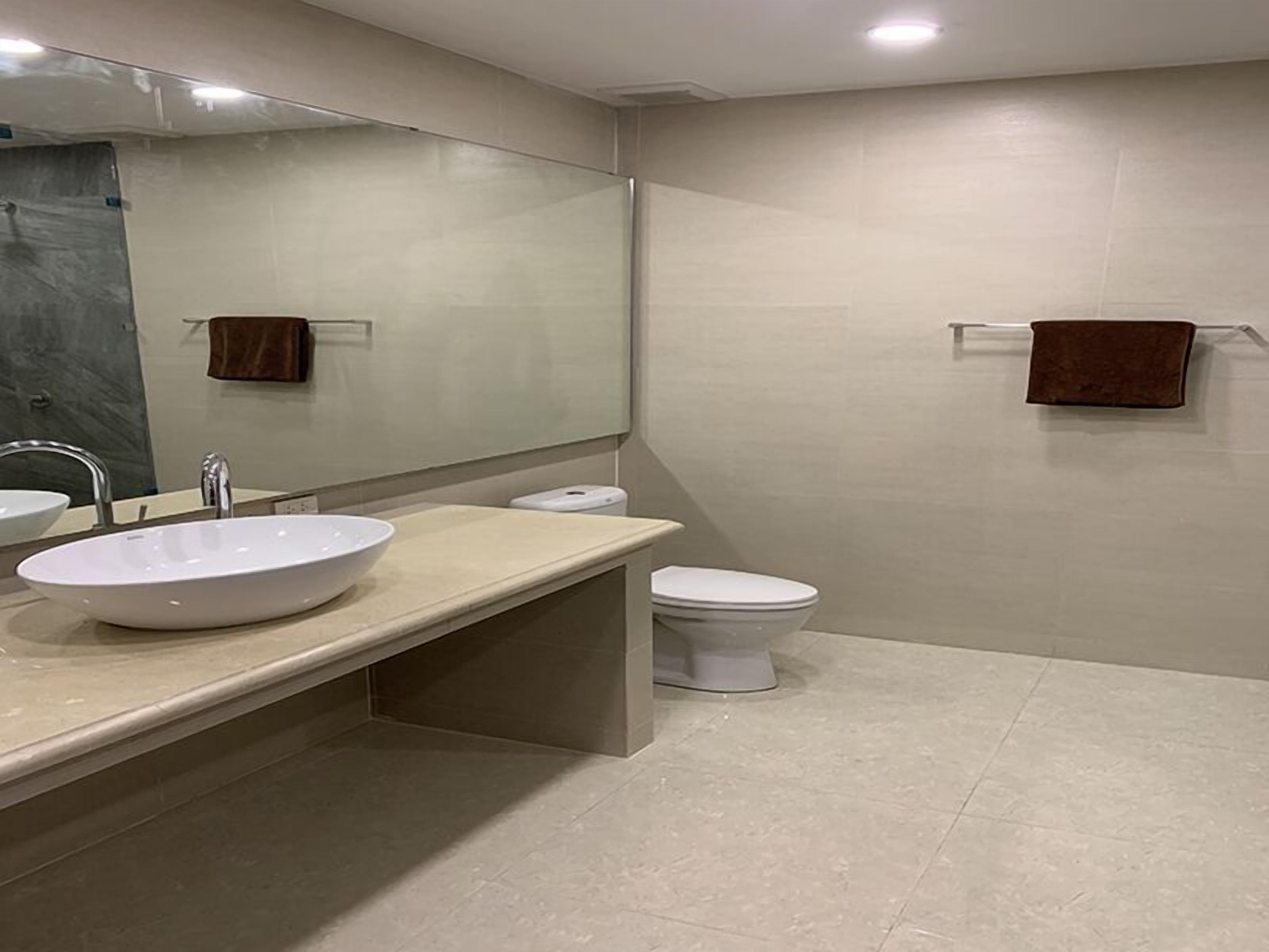 A modern bathroom with a large mirror, a white sink, and a toilet.