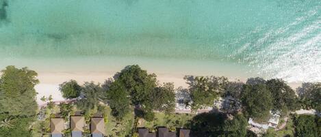 An aerial view of a beachfront property with several buildings, a sandy beach, and dense greenery.