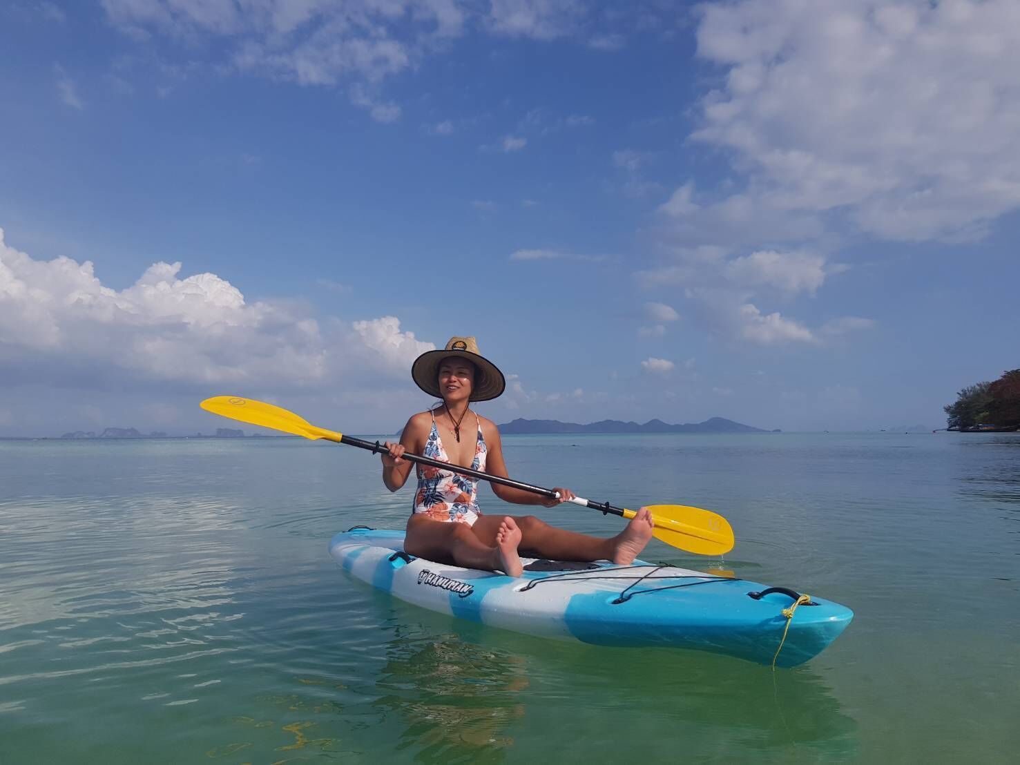 A person kayaking on a clear day with calm waters and distant mountains.