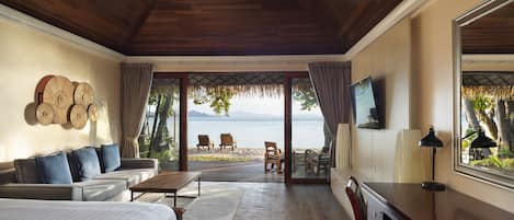 Una habitación amplia con techo de madera, una cama grande, un sofá, un escritorio y vistas al mar a través de amplias ventanas.