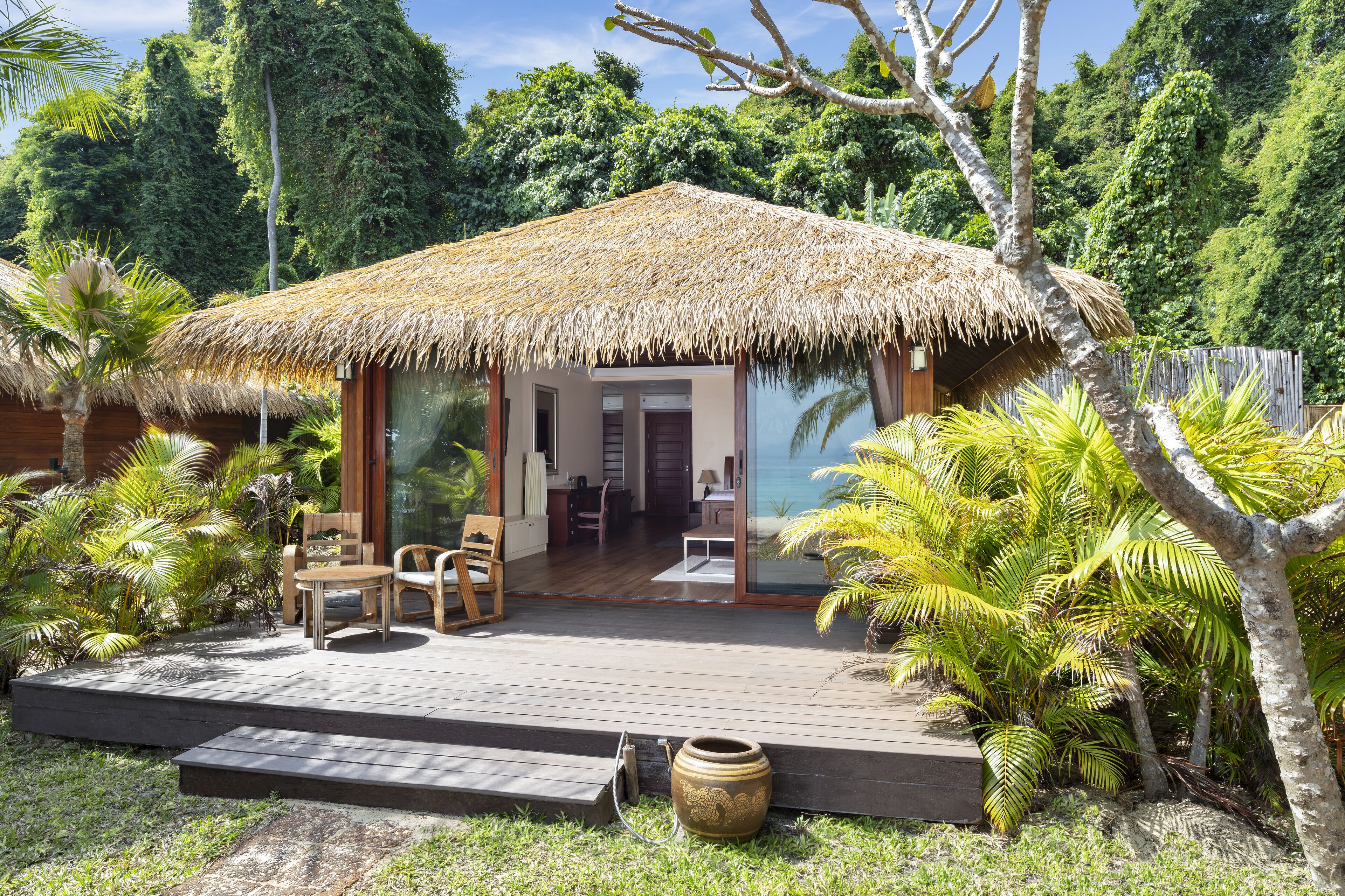 A thatched-roof hut with a wooden deck, surrounded by tropical vegetation.