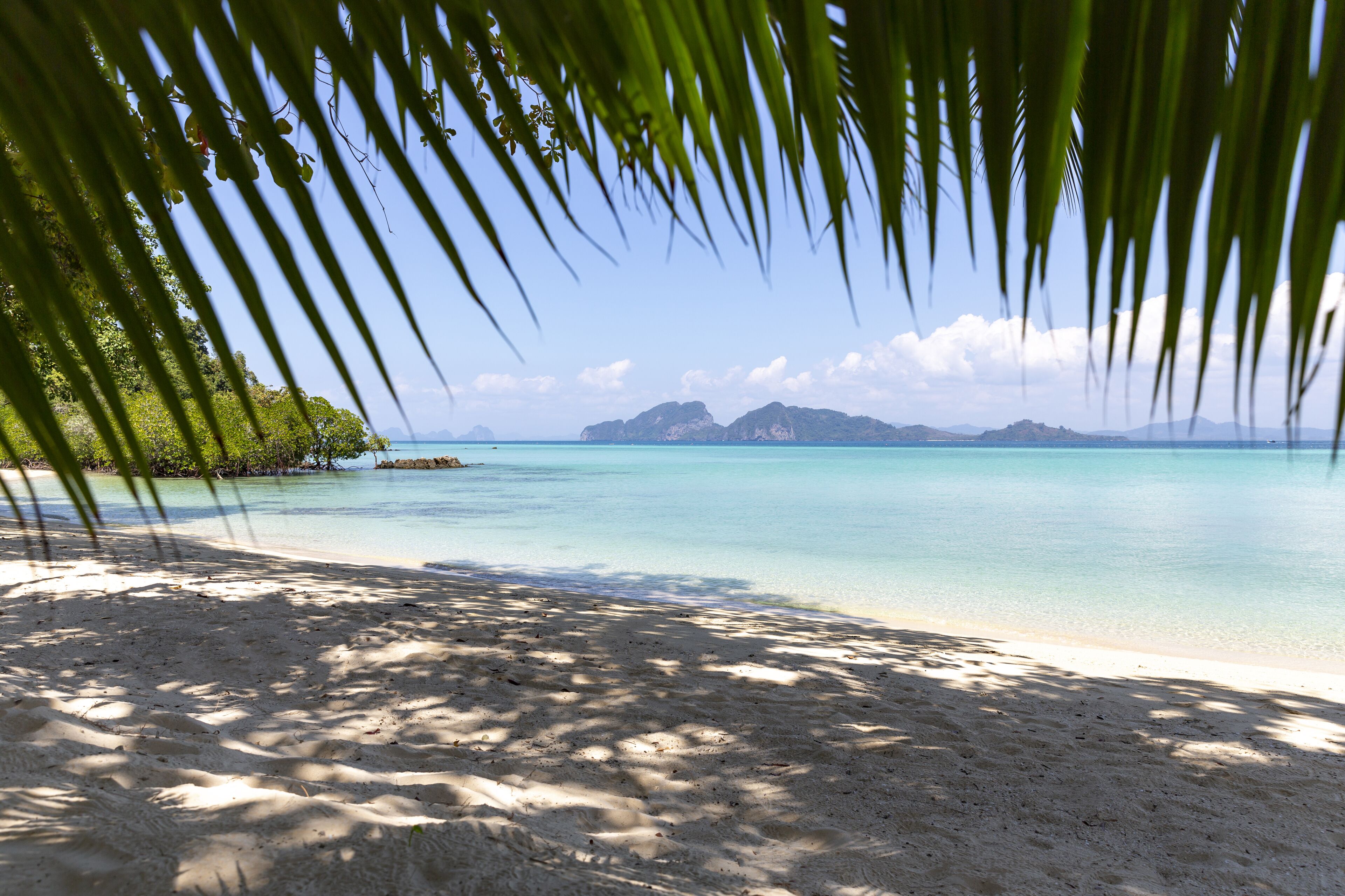 A beach with clear turquoise water, sandy shore, and distant mountains.