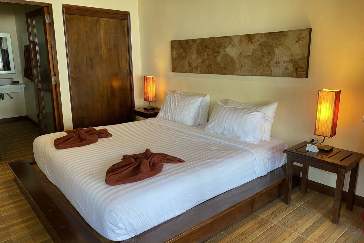 A hotel room with a large bed, two bedside lamps, a wooden headboard, and a mirror above the bed.