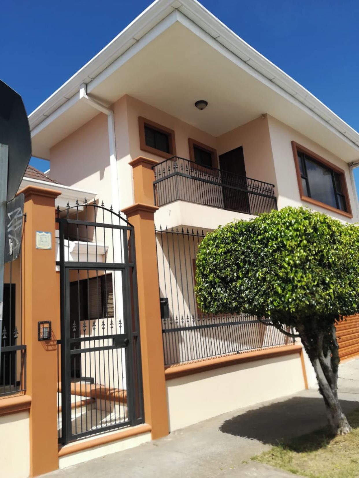 Une maison à deux étages avec une entrée fermée par un portail, un balcon et une haie bien entretenue.
