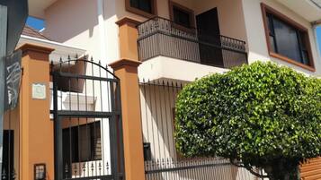 Une maison à deux étages avec une entrée fermée par un portail, un balcon et une haie bien entretenue.