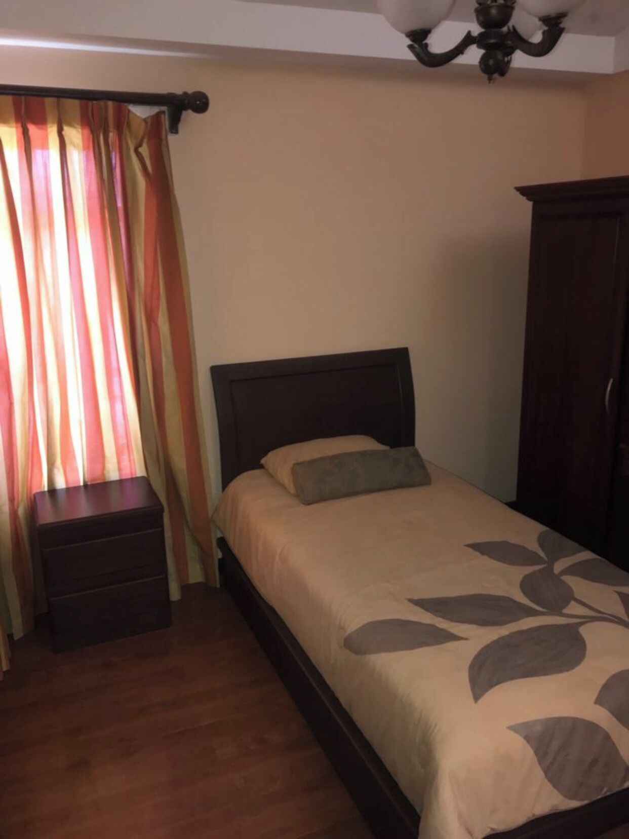 Een slaapkamer met een bed, nachtkastje, kledingkast en een raam met gordijnen.