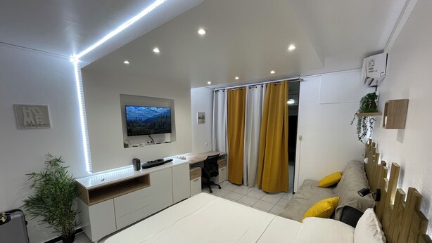 Quarto moderno com cama, escrivaninha e televisão na parede.