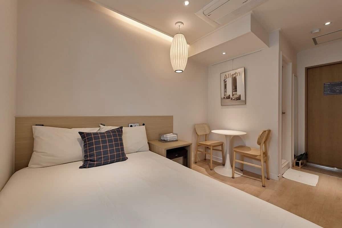 Una habitación de hotel moderna con una cama grande, una mesita de noche, una silla, una pequeña mesa y una obra de arte colgada en la pared.