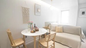 Una sala de estar moderna y minimalista con una mesa redonda blanca, dos sillas de madera, un sofá color beige y un tapiz de macramé en la pared.