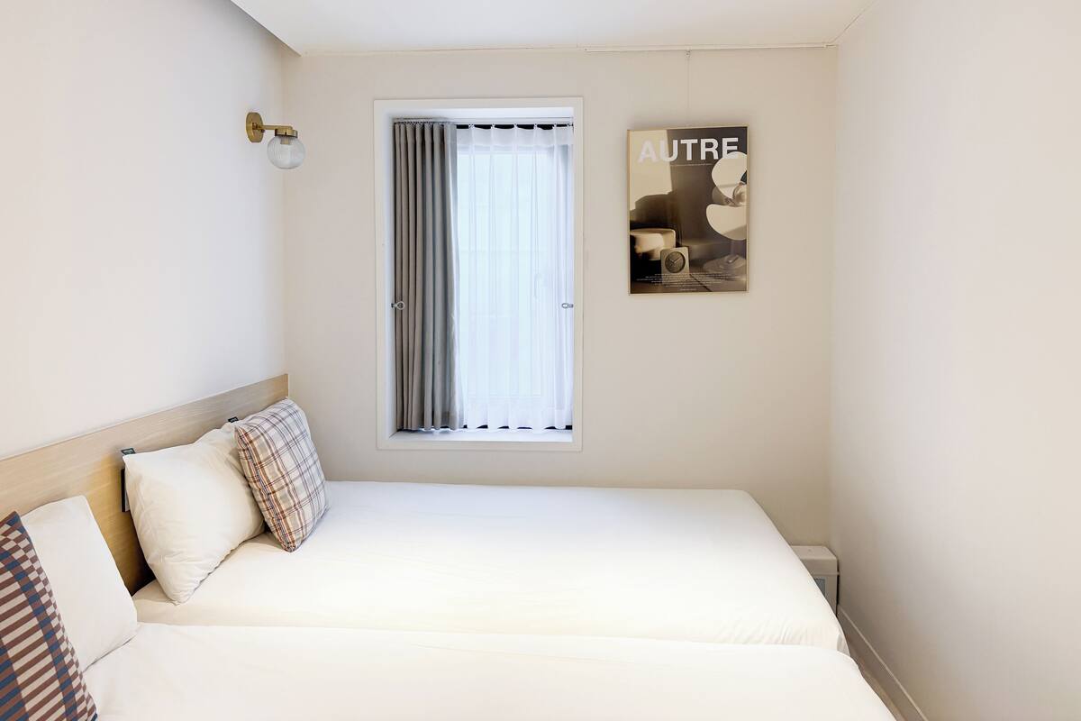 Un dormitorio con cama, ventana con cortinas, una lámpara de pared y un cartel.