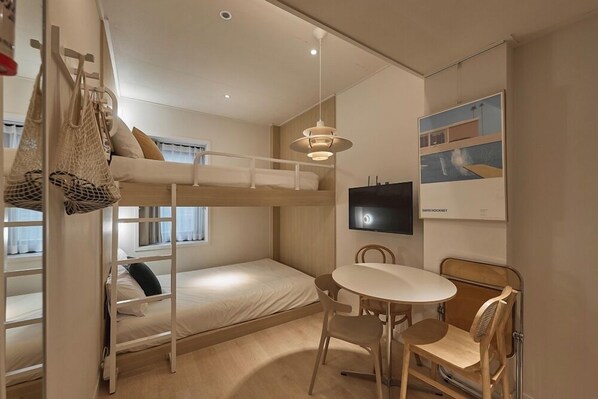 A bunk bed room with a desk and chairs, a hanging bag, and a TV on the wall. - Artravel Home (Seoul)