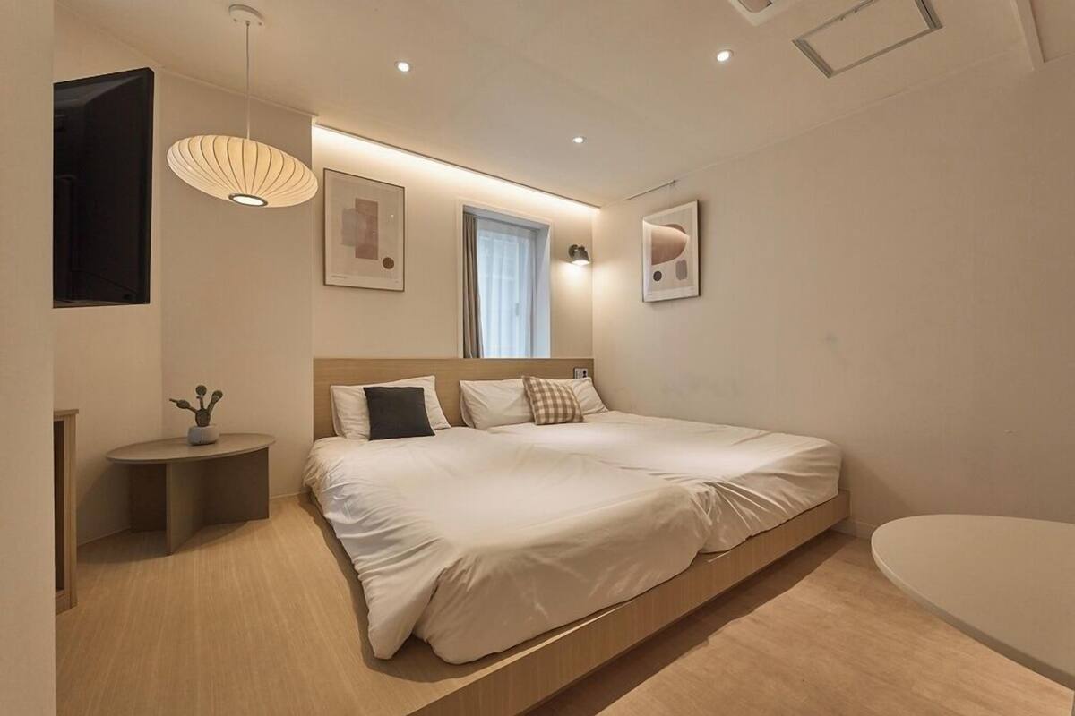 Un dormitorio moderno con una cama grande, mesitas de noche, un banco empotrado y una pequeña mesa redonda con una planta.