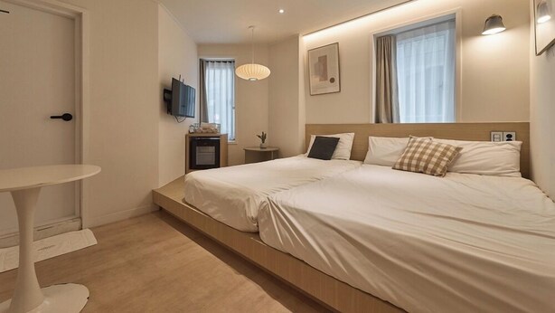 Una habitación de hotel moderna con una cama grande, una mesita de noche pequeña, un televisor montado en la pared y un ventanal con cortinas.
