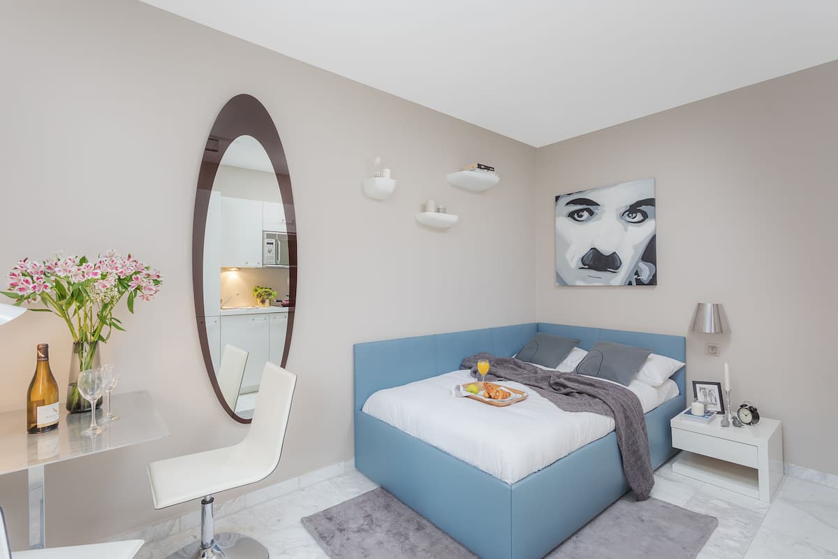 A modern bedroom with a blue bed, white bedside table, and a large mirror.