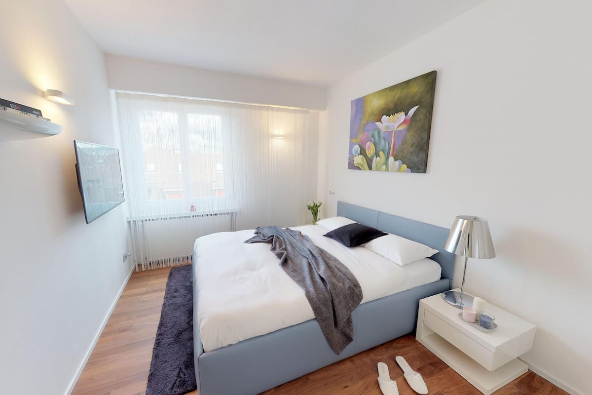 A modern bedroom with a bed, bedside table, and a painting.
