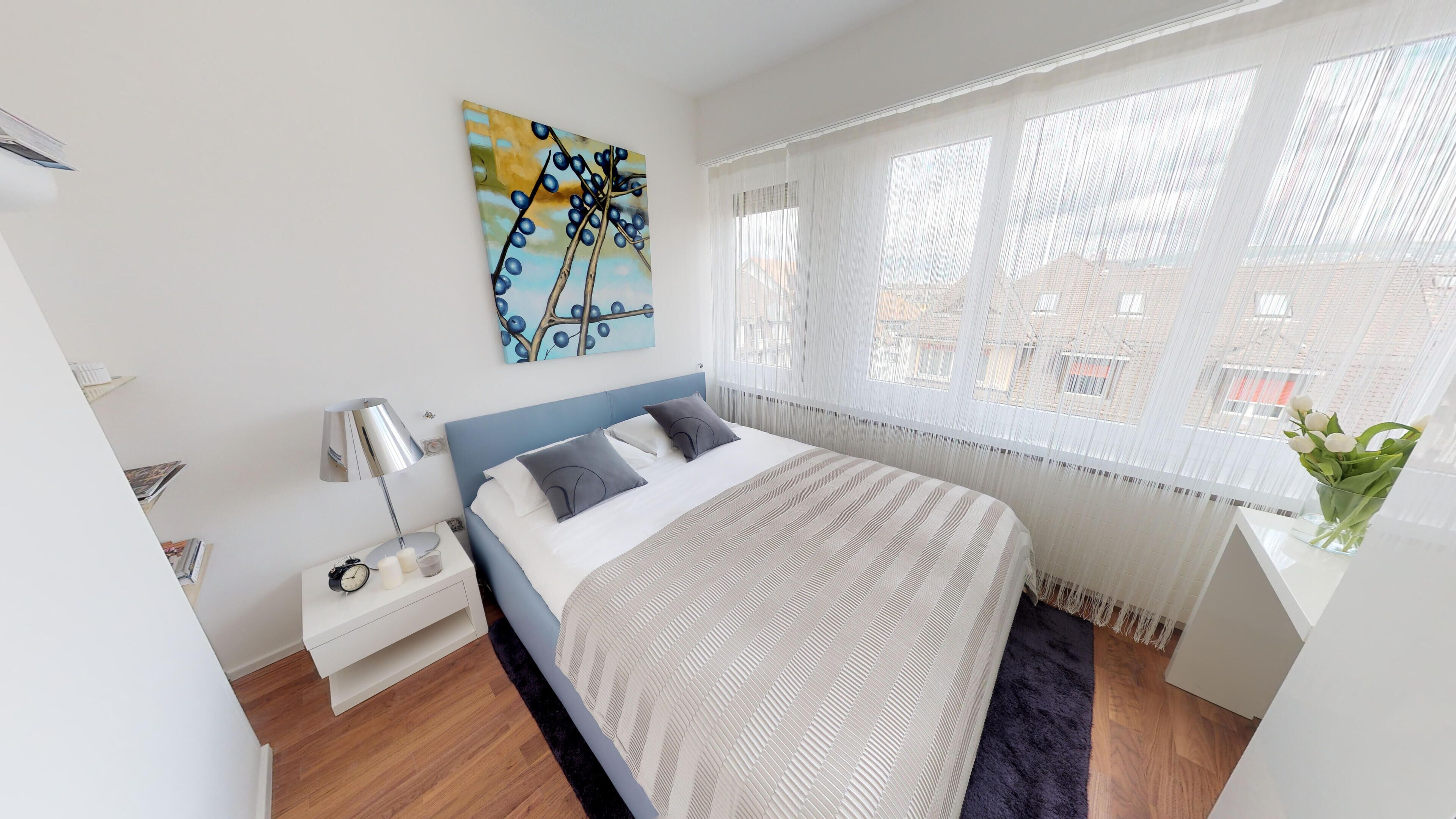 A modern bedroom with a bed, bedside table, lamp, and a painting on the wall.