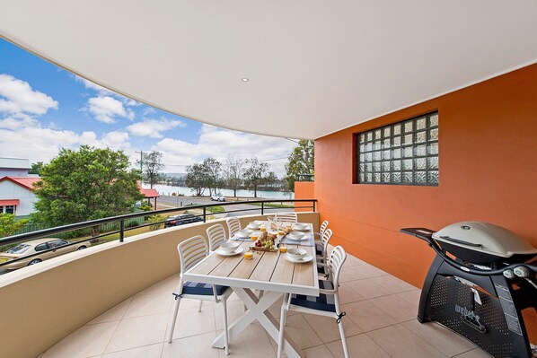 A balcony with a table set for breakfast, a grill, and a view of a lake and buildings.