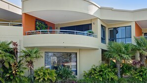 A modern multi-story building with balconies, large windows, and lush tropical plants.