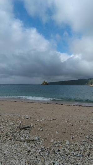 Una playa rocosa con una pequeña isla a lo lejos.