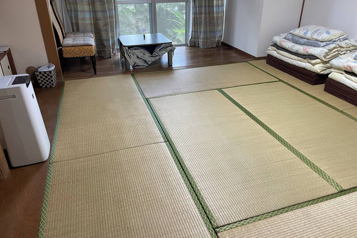 Ein Zimmer mit Tatami-Matten, einem Futon, einem kleinen Tisch und einem Heizgerät.