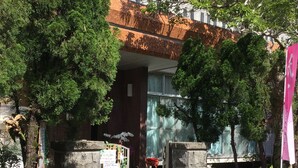 Un edificio con fachada de ladrillo y tejado de tejas, rodeado de árboles y plantas en macetas.
