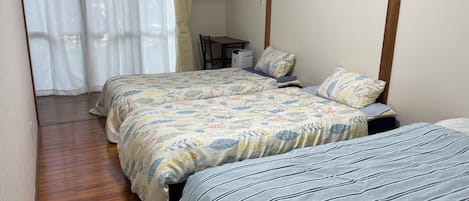 A room with two beds, a wooden floor, a chair, and a table.