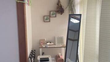 A room with a wooden floor, a white air purifier, a mirror, a shelf with toiletries, and a window with blinds.