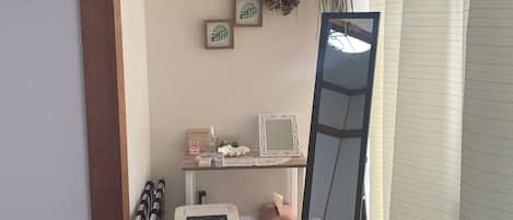 A room with a wooden floor, a white air purifier, a mirror, a shelf with toiletries, and a window with blinds.