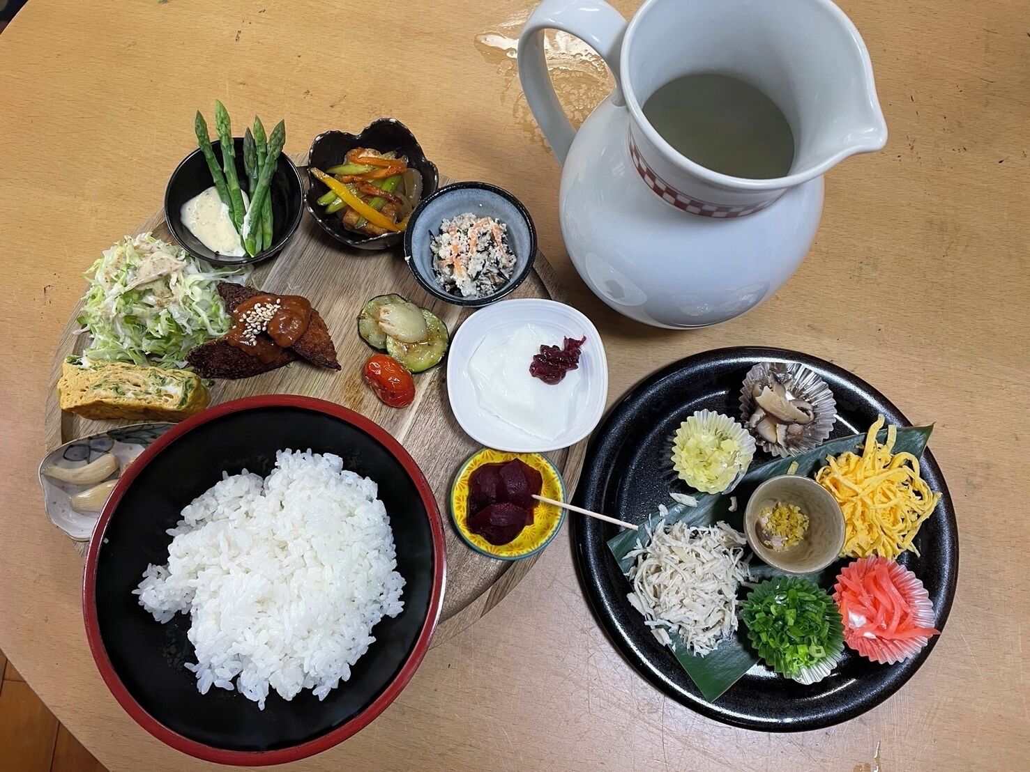 A table with various dishes including rice, vegetables, and a pitcher of water.