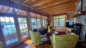 A cozy living room with a stone fireplace, wooden floors, and large windows overlooking a body of water.