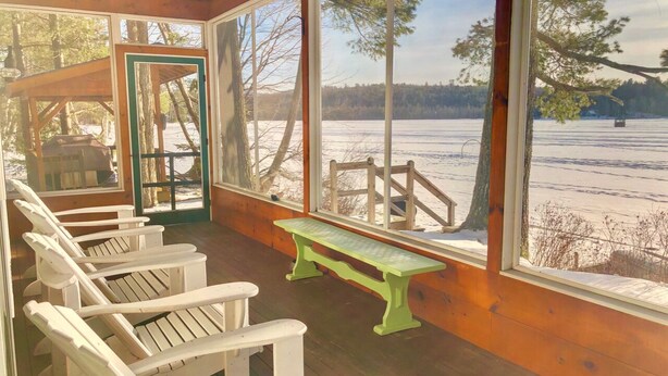 A covered outdoor seating area with Adirondack chairs and a bench, overlooking a snowy landscape.