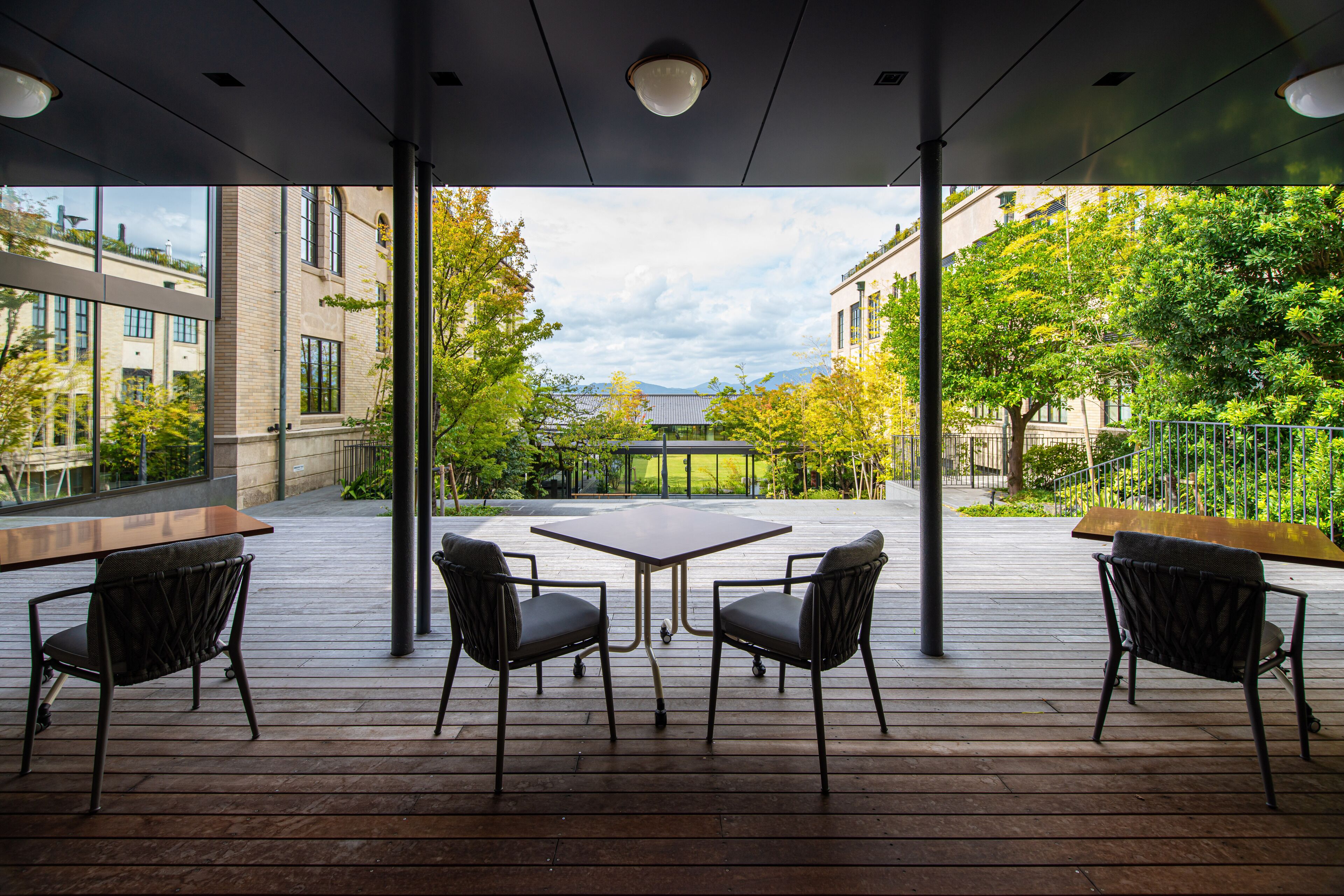 An outdoor patio with a table and chairs, large windows, and a view of buildings and trees.