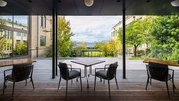 Un patio al aire libre con mesa y sillas, ventanas amplias y vistas a edificios y árboles.