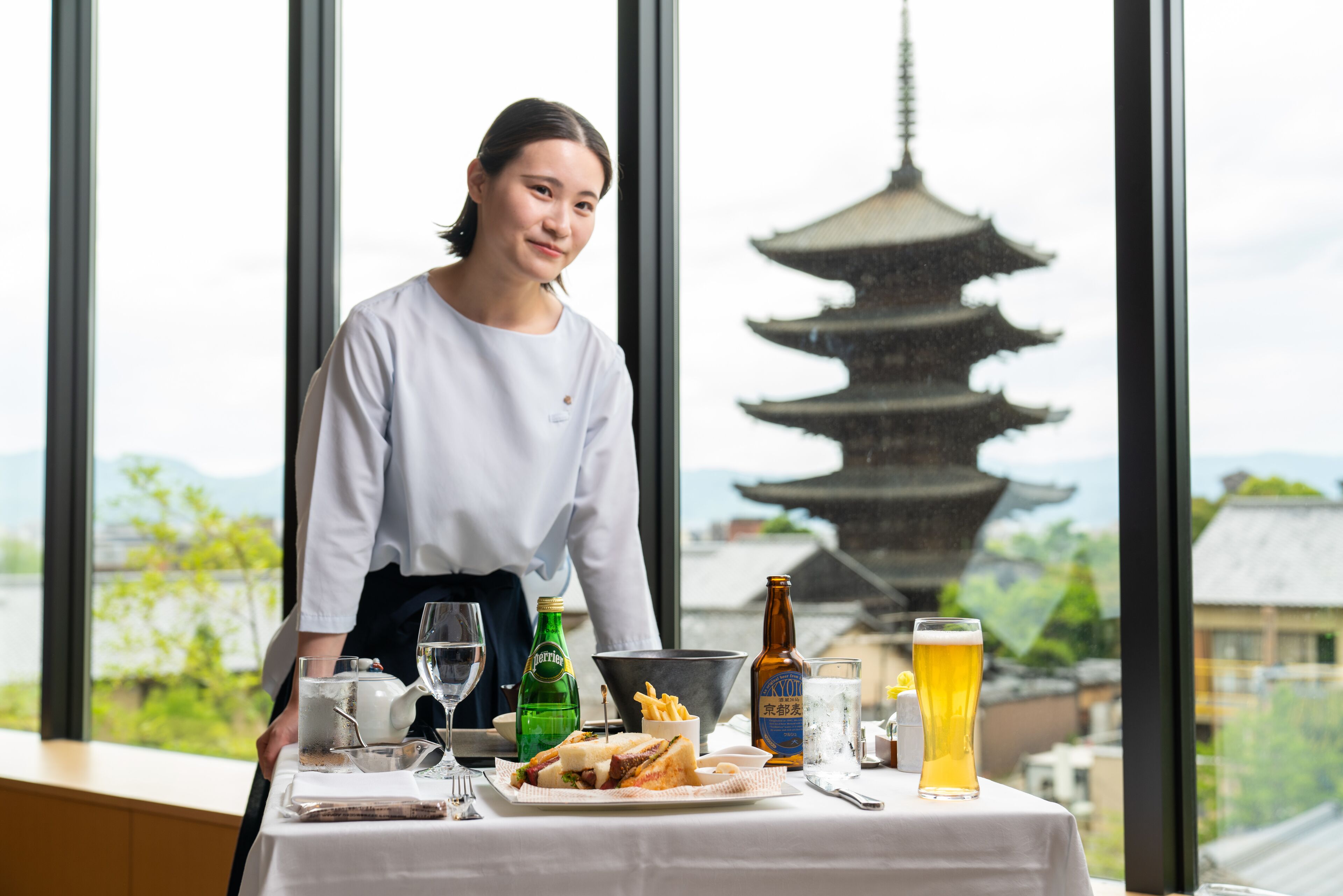 A table set with a meal, drinks, and a view of a pagoda through a window.