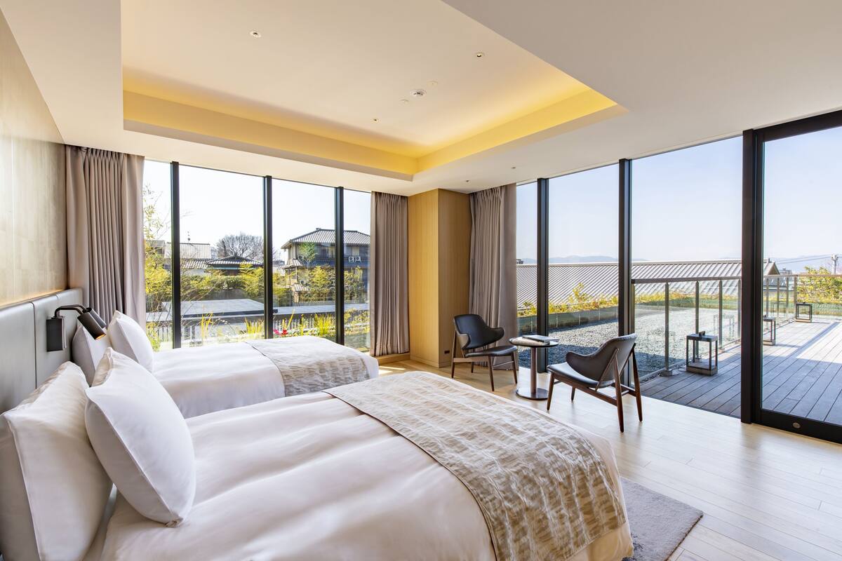 Une chambre d’hôtel moderne avec deux lits, un balcon et de grandes fenêtres donnant sur la ville.