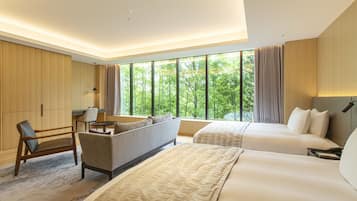 A modern hotel room with a large bed, a sofa, a desk, and a view of greenery through large windows.