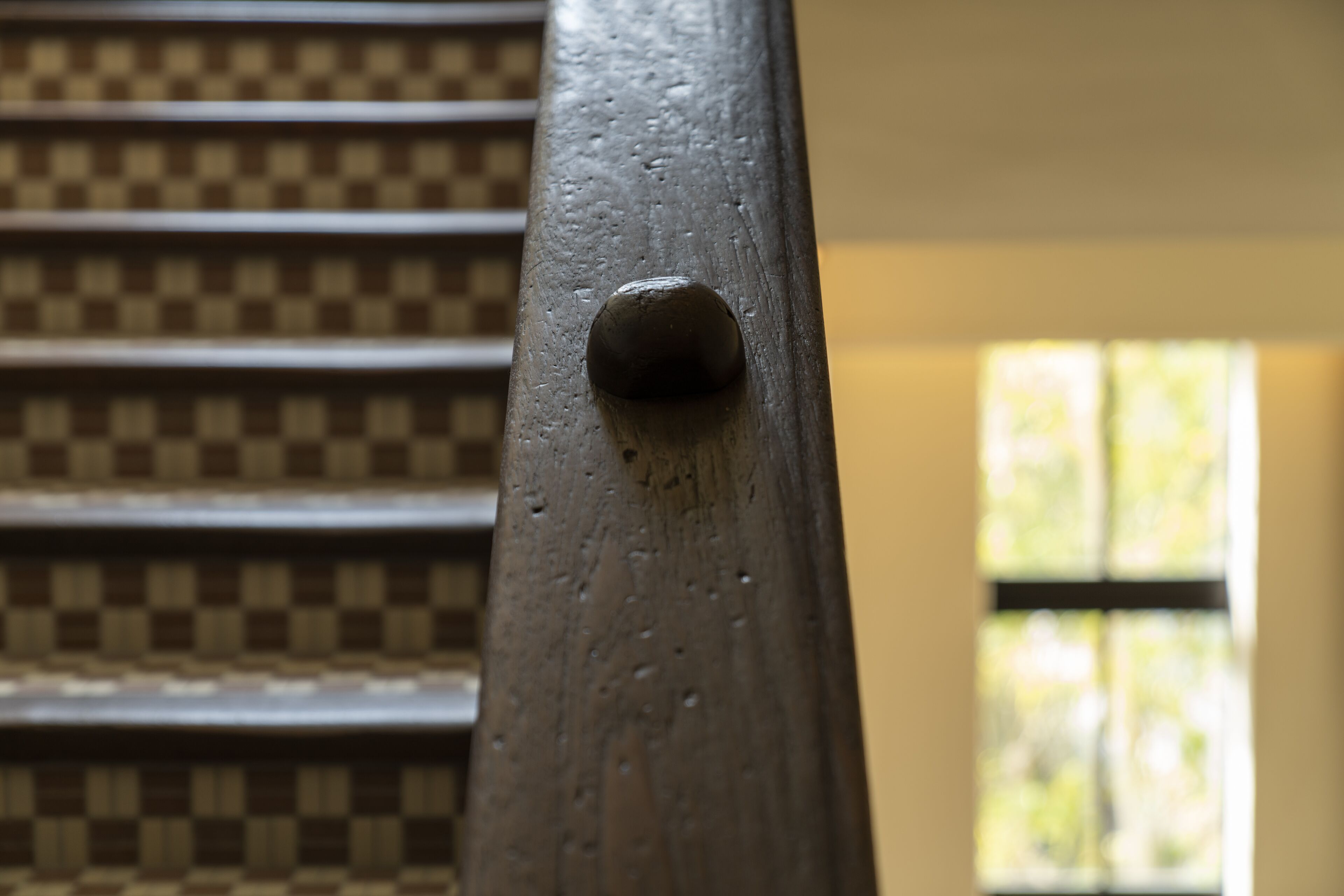 A close-up of a wooden chair with a checkered pattern upholstery and a metal armrest.
