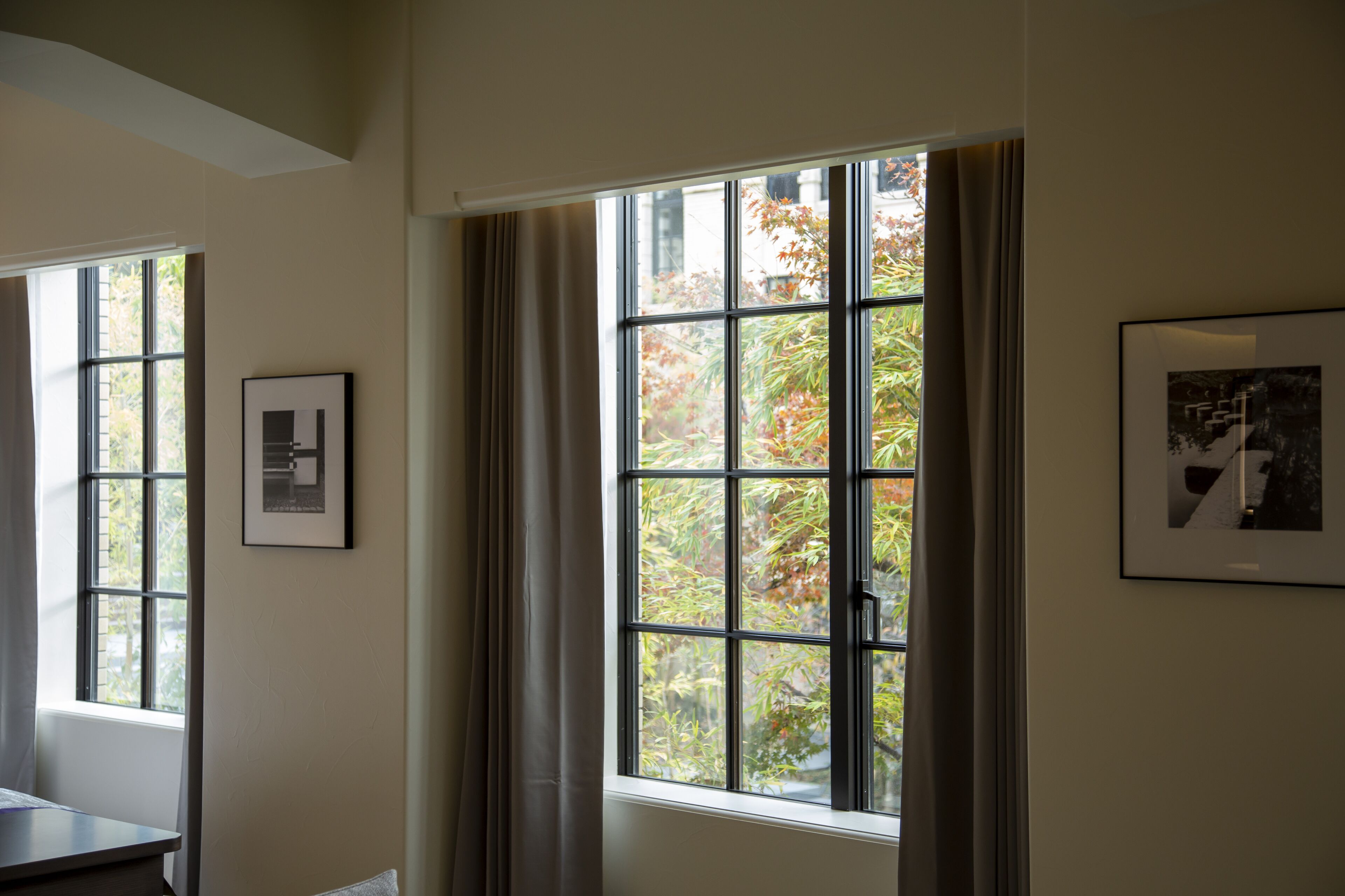 A room with large windows, framed artwork on the walls, and a view of trees outside.