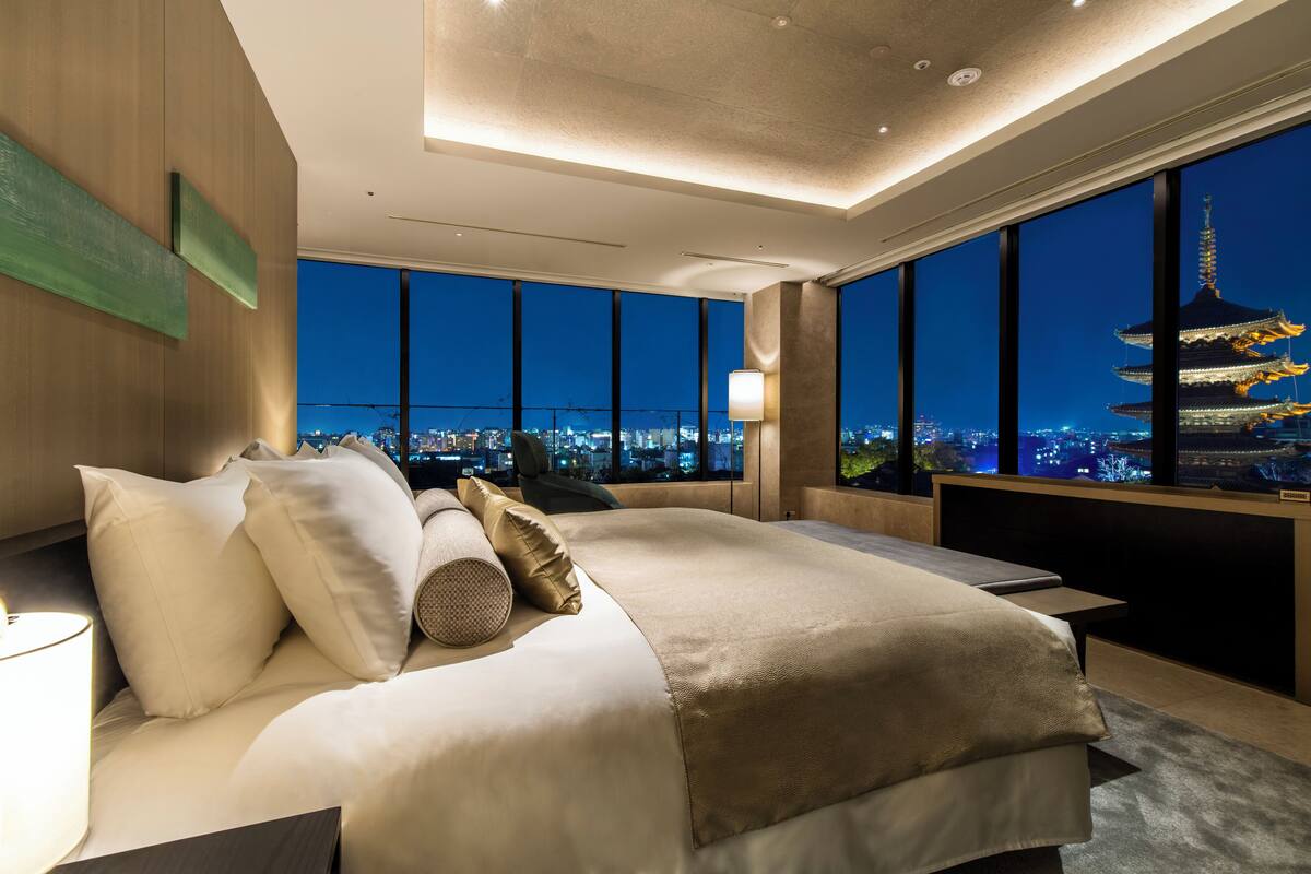 Une chambre d’hôtel moderne avec un grand lit, une table de chevet et une vue sur le paysage urbain et une pagode.
