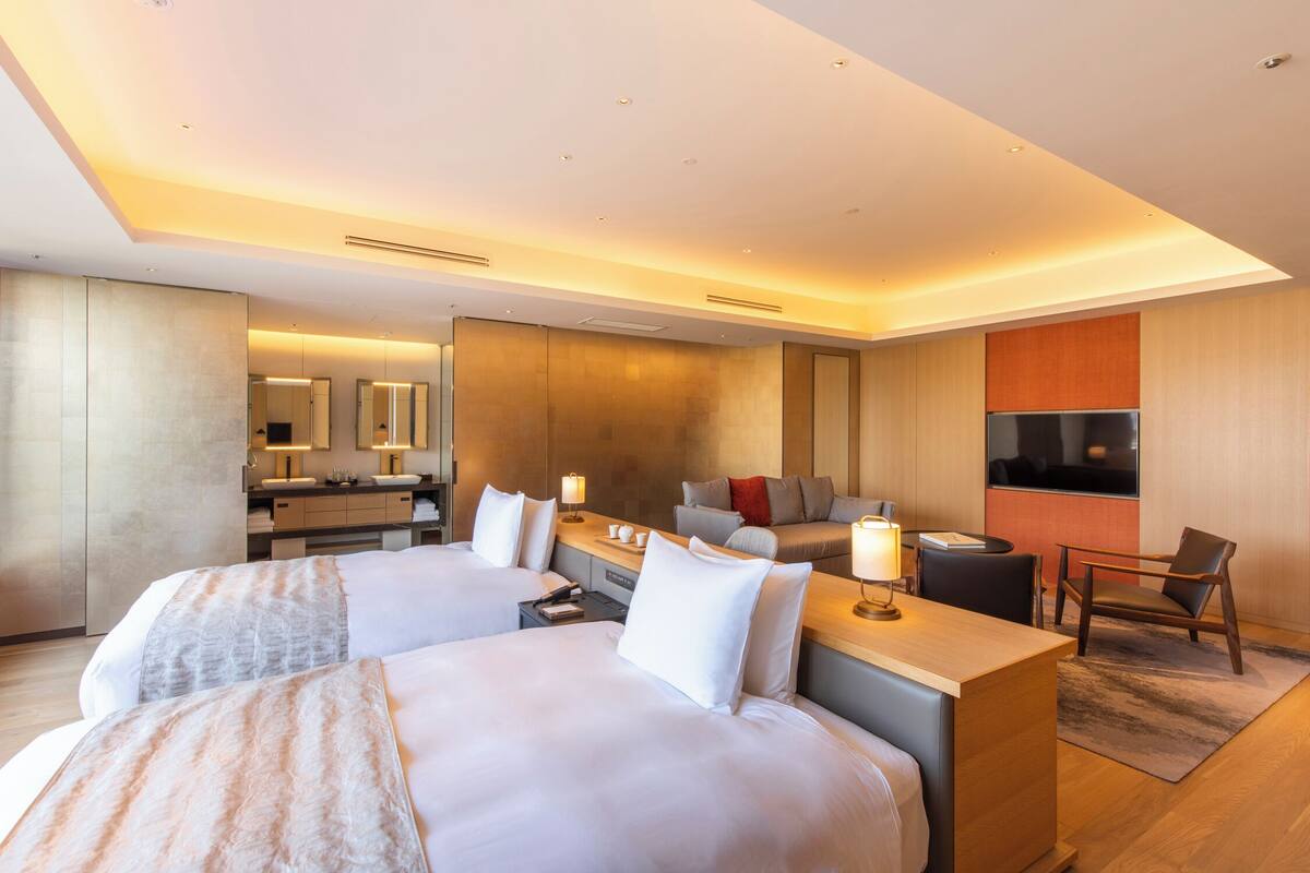 Une chambre d’hôtel moderne équipée de deux lits, d’un bureau, d’un canapé, d’une télévision et d’une salle de bain avec un miroir et un lavabo.