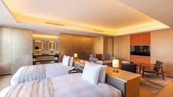 Una habitación de hotel moderna con dos camas, un escritorio, un sofá, un televisor y un baño con espejo y lavamanos.
