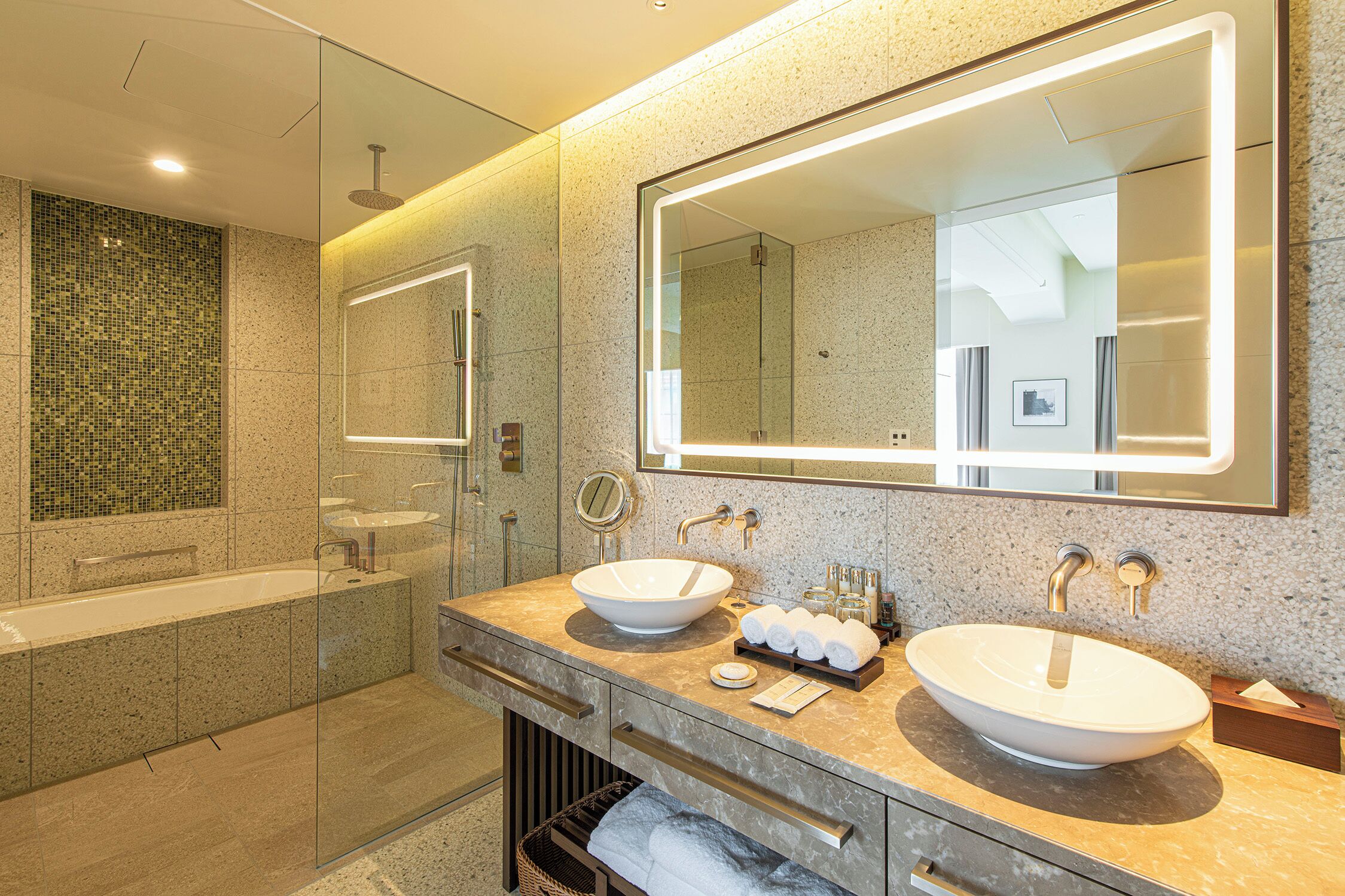 Un baño moderno con un espejo grande, dos lavamanos, una bañera y una ducha con cerramiento de vidrio.