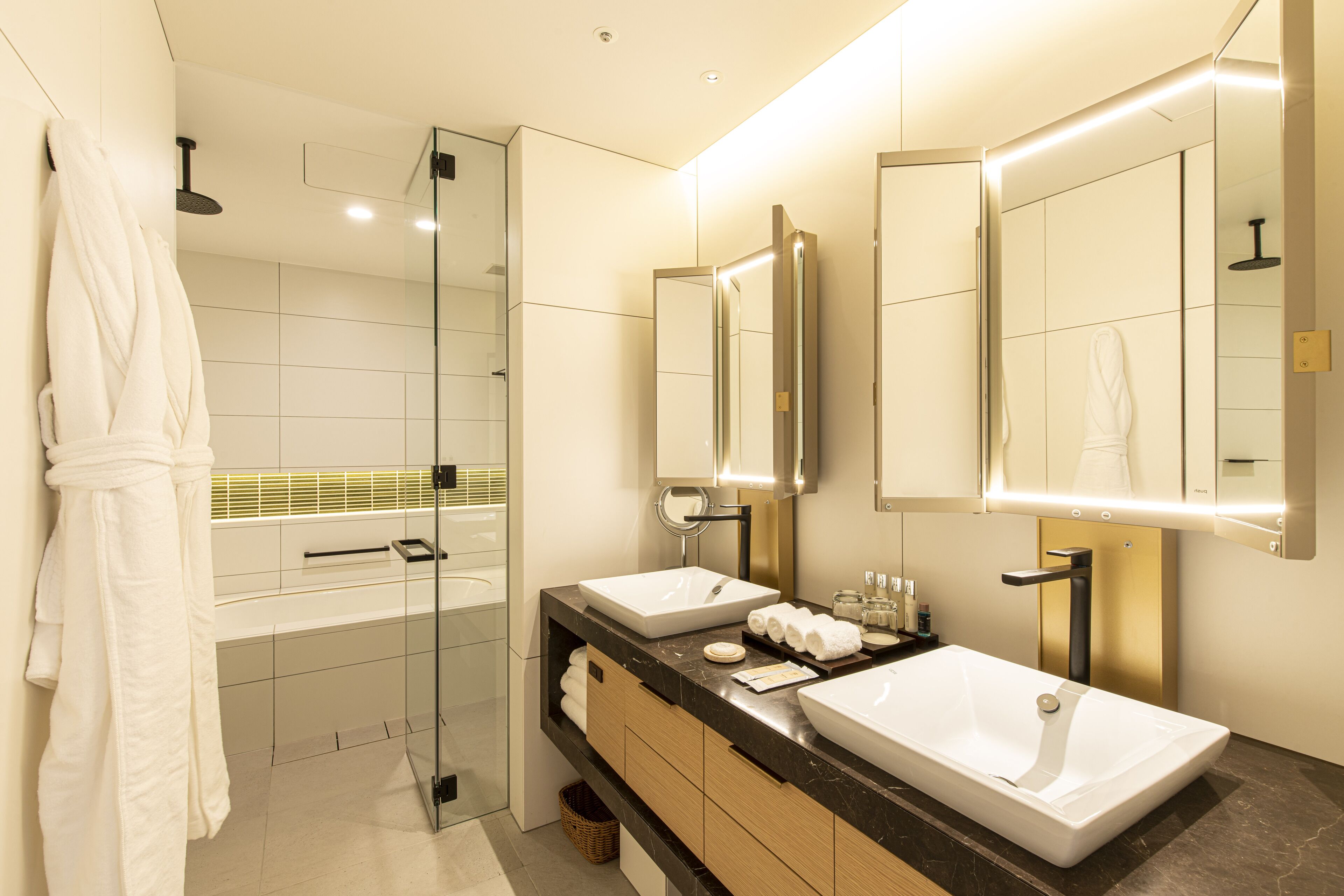 A modern bathroom with two sinks, a glass shower enclosure, and a robe hanging on the wall.
